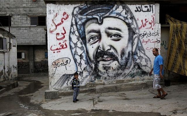 Palestinians walk past a mural depicting late Palestinian leader Yasser Arafat at the Shati Refugee Camp, in Gaza City, on November 7, 2013 (AP/Adel Hana)