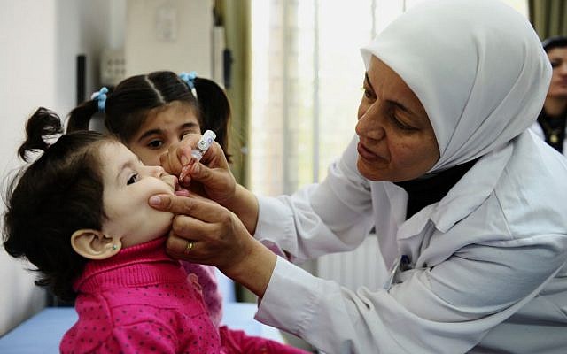 A health worker administers polio vaccine to a child as part of a UNICEF-supported vaccination campaign at the Abou Dhar Al Ghifari Primary Health Care Center in Damascus, Syria. (photo credit: AP/UNICEF, Omar Sanadiki)