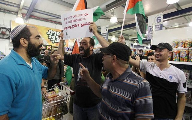 Palestinian protesters hold up flags and a sign reading "boycott occupation and its products" during a protest at a Rami Levy supermarket in the West Bank Jewish settlement of Modiin Illit, October 24, 2012 (photo credit: Issam Rimawi/Flash90)
