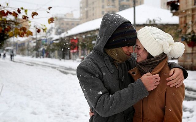 An Israeli couple keeps warm in the snow on Jaffa Street along the light rail tracks in central Jerusalem, on the third day of the major snowstorm that hit the capital, Saturday, December 14, 2013. (photo credit: Hadas Parush/Flash 90)