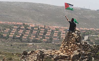 A man waves a Palestinian flag waves near the West Bank settlement of Ofra, near Ramallah (photo credit: Issam Rimawi/Flash90)