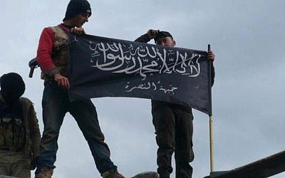 January 2013 citizen journalism image shows rebels from al-Qaeda-affiliated al-Nusra Front waving their brigade flag on top of a Syrian air force helicopter, at Taftanaz air base, captured by the rebels, in Idlib province, northern Syria. (photo credit: AP/Edlib News Network ENN, File)