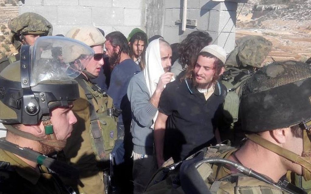 Meir Ettinger, wearing a white skullcap, is escorted by IDF soldiers out of the  West Bank village of Qusra, January 7, 2014. (Rabbis for Human Rights)