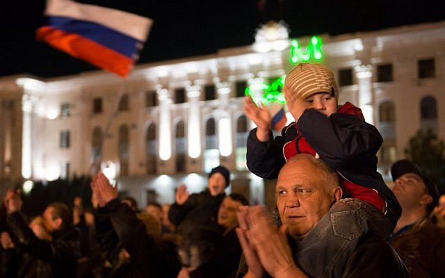 A young boy sits on the shoulders of an elderly man at a parade in the center of the Crimean city of Simferopol on March 21, 2014, after Russia's upper house of parliament unanimously voted to ratify the treaty incorporating Crimea into Russian territory. (photo credit: AFP/ Dmitry Serebryakov)