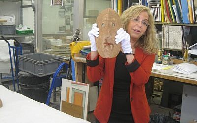Dr. Debby Hershman, curator of prehistoric culture at the Israel Museum, holds up a neolithic mask in the museum's laboratories. (photo credit: Ilan Ben Zion/Times of Israel staff)