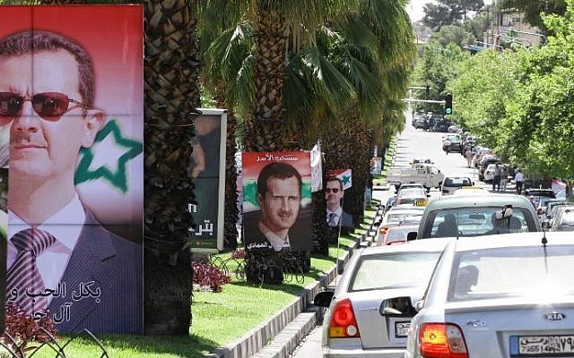 Syrians drive past election campaign posters bearing portraits of President Bashar Assad on May 18, 2014 in the capital Damascus. Campaigning began last week for Syria's June 3 presidential election expected to return Assad to power. (photo credit: Louai Beshara/AFP)