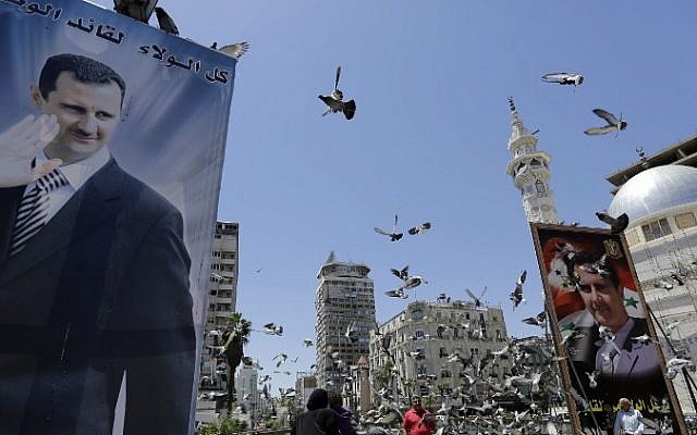 Syrians feed pigeons on a square where are displayed giant campaign billboards bearing portraits of Syrian President Bashar Assad on June 1, 2014 in the capital Damascus. (Photo credit: AFP/Joseph Eid)