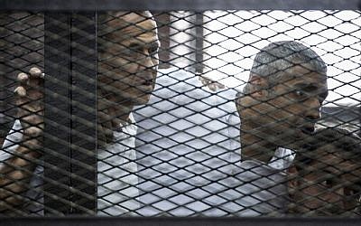 Al-Jazeera news channel's Australian journalist Peter Greste (L) and his colleagues, Egyptian-Canadian Mohamed Fadel Fahmy (C) and Egyptian Baher Mohamed , listen to the verdict inside the defendants cage during their trial for allegedly supporting the Muslim Brotherhood on June 23, 2014 at the police institute near Cairo's Tora prison. (photo credit: AFP Photo/Khaled Desouki)