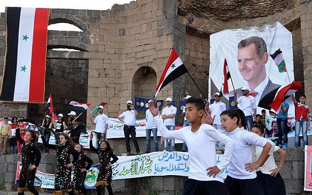 Supporters of Syrian President Bashar Assad hold his portraits and wave Syrian flags during a demonstration in support of his candidacy for presidential election in Suweida town, southern Syria, May 31 2014 (Photo credit: AP Photo/SANA)