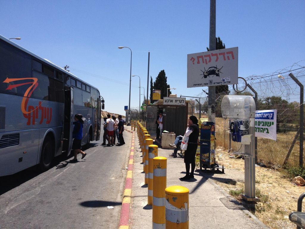 A public bus pulling up at the trempiada, while others continue to wait for other options in the hot sun (photo credit: Jessica Steinberg/Times of Israel)