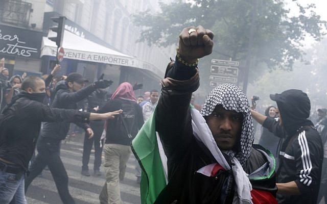 A protester wearing a kaffiyeh and wrapped in a Palestinian flag raises his fist on July 13, 2014 in Paris, during a demonstration against Israel and in support of residents in the Gaza Strip. (photo credit: AFP/KENZO TRIBOUILLARD)