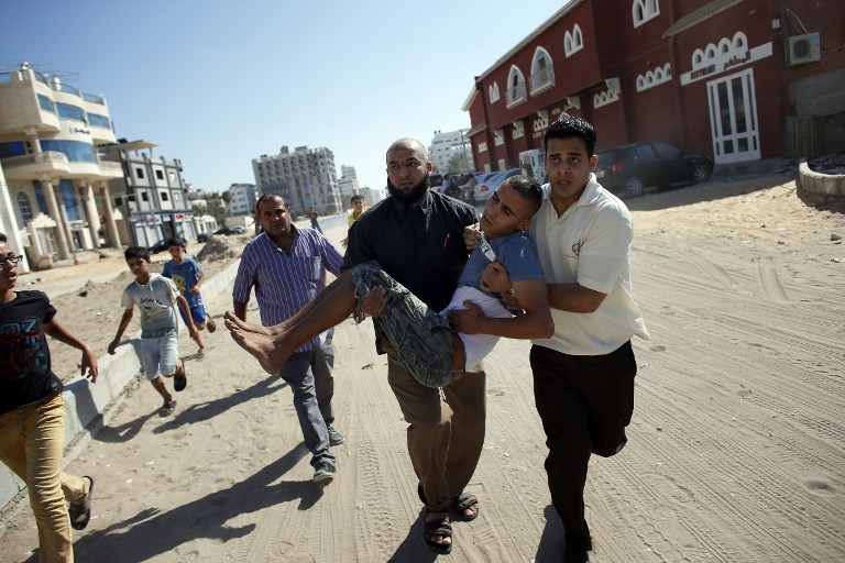 Palestinian employees of Gaza City's al-Deira hotel carry a wounded boy following an Israeli military strike near on the beach, on July 16, 2014. Four children were killed in Gaza City during the attack. (photo credit: AFP/THOMAS COEX)
