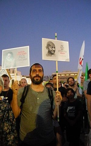 A protester holds a sign in Hebrew with Ghandi's face and the quote "An eye for an eye leaves the whole world blind," Tel Aviv, July 03, 2014. (photo credit: Melanie Lidman)