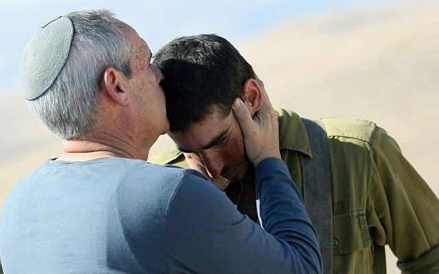 A religious Jewish father kisses his son on the forehead.