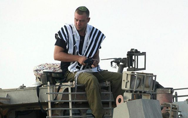 An IDF soldier prays atop an armored IDF bulldozer near the Gaza border in southern Israel on the first day of Operation Protective Edge, July 8, 2014. (photo credit: David Buimovitch/Flash90)