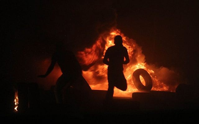 Palestinian men burning tires during clashes with Israeli border police at the Qalandiya checkpoint, between Jerusalem and Ramallah, late on July 24, 2014, following a massive march attended by 10,000 Palestinian protesters against Israel's military offensive in the Gaza Strip. (photo credit: Issam Rimawi/FLASH90)
