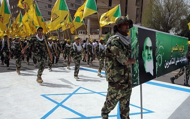 Illustrative: Iraqi Hezbollah members hold up the yellow flags of the Iraqi branch of the Lebanese terror group and a portrait of Iran's late supreme leader, Ayatollah Ruhollah Khomeini, as they walk on an Israeli flag painted on the ground during a parade marking al-Quds (Jerusalem) International Day on July 25, 2014, in the Iraqi capital Baghdad. (AFP/Ali al-Saadi)