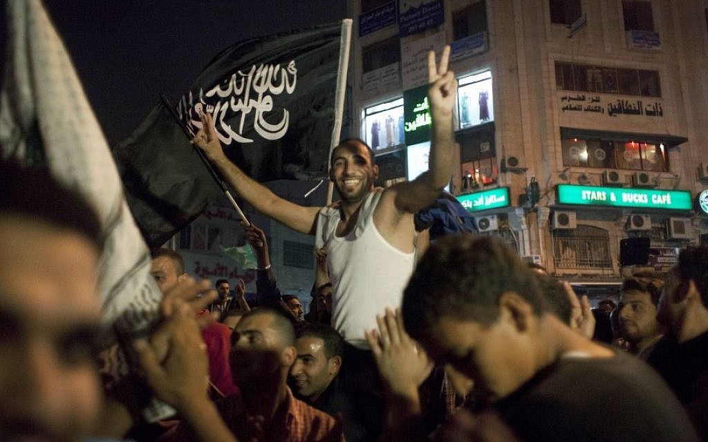 Palestinians dance while flying a Palestinian Islamic Jihad Movement flag reading in Arabic "there is only one God and Muhammad is his prophet," during celebrations in the West Bank city of Ramallah, late Sunday, July 20, 2014.  (photo credit: AP Photo/Nasser Nasser)