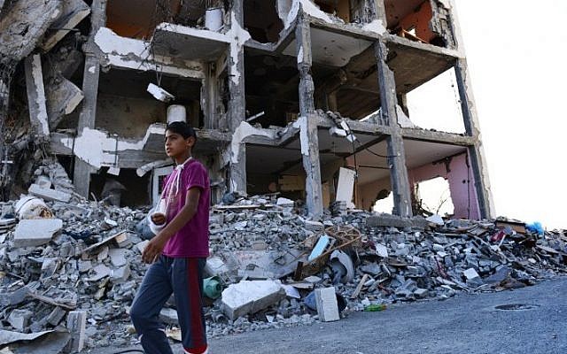 Feras Abu Inil, 13, walks past an apartment block in the northern Gaza strip that was all but destroyed in four weeks of clashes between Israel and Hamas, Wednesday, August 13, 2014. (photo credit: Roberto Schmidt/AFP)