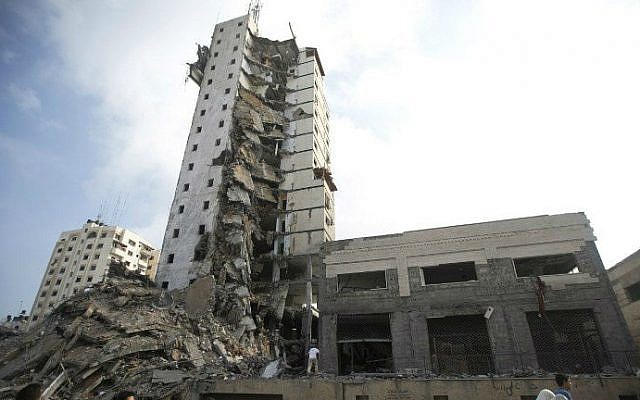 Palestinians look up at the remains of an apartment tower block that Israel said was used by Hamas as a command center and that was destroyed by an Israeli airstrike overnight in Gaza City on August 26, 2014. (photo credit: AFP/MAHMUD HAMS)