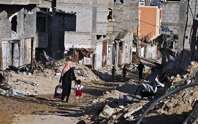 A Palestinian woman holds the hand of a child as they head home with some of their belongings on August 27, 2014, in Gaza City's Shejaiya neighborhood. (photo credit: AFP/Robert Schmidt)