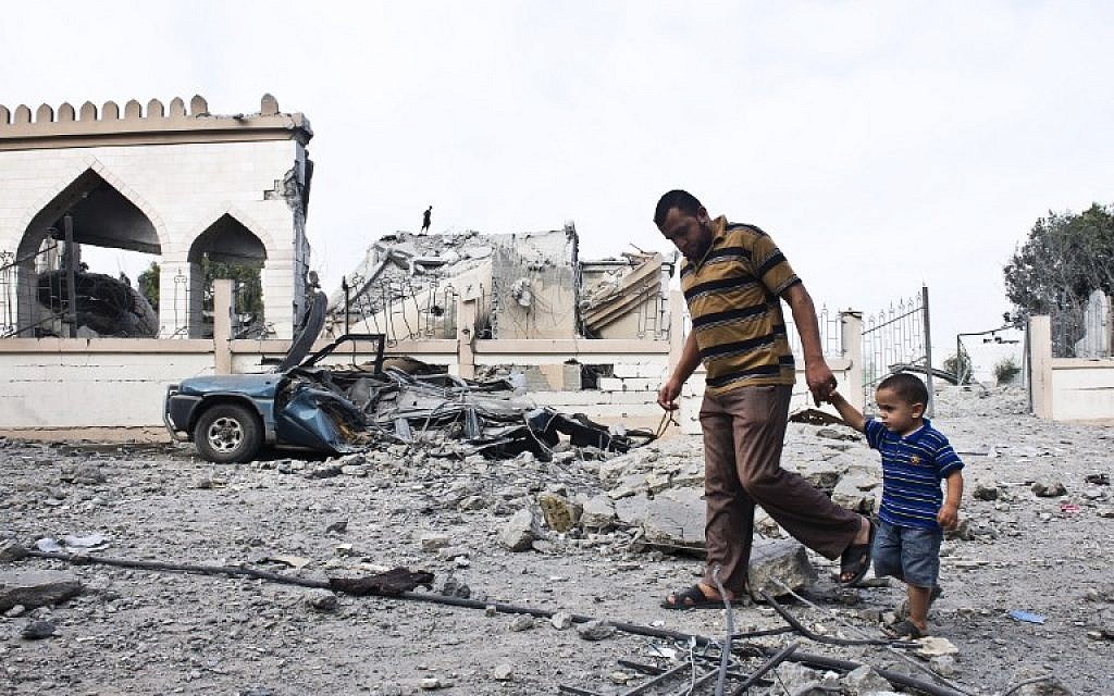 A Palestinian man walks with a child past the rubble of a mosque that was partially damaged by an Israeli airstrike on August 25, 2014 in Beit Lahia in the northern Gaza Strip. (photo credit: AFP/ROBERTO SCHMIDT)