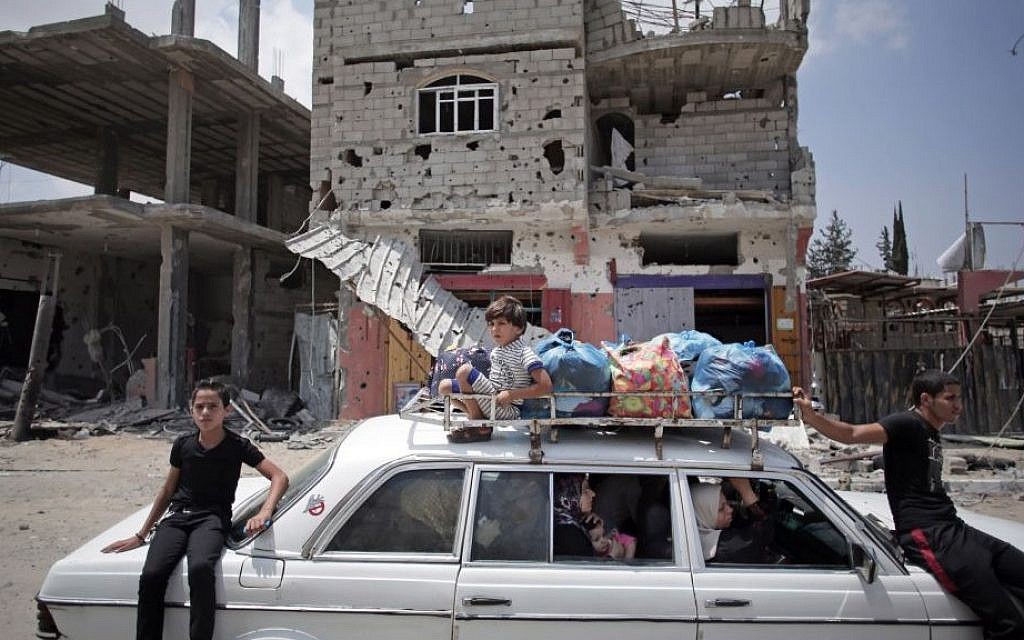 Palestinians in a car with their belongings drive past a destroyed house in Rafah's district of Shawkah in the southern Gaza Strip, Tuesday, Aug. 5, 2014. (photo credit: AP/Khalil Hamra)