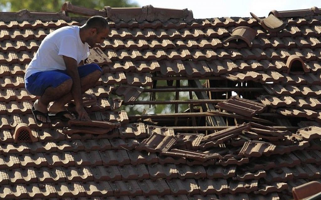 An Israeli man examines the damage to the roof of his house after a rocket fired from Gaza hit in a residential neighborhood of the southern city of Sderot, Friday, August 8, 2014. (photo credit: AP Photo/Tsafrir Abayov)