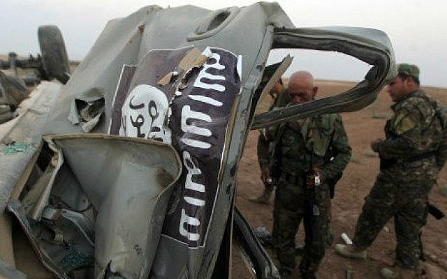 Peshmerga fighters inspect the remains of a car, bearing an image of the trademark jihadist flag, which belonged to Islamic State (IS) militants after it was targeted by an American air strike in the village of Baqufa, north of Mosul, on August 18,2014 (photo credit: AFP/Ahmad al-Rubaye)