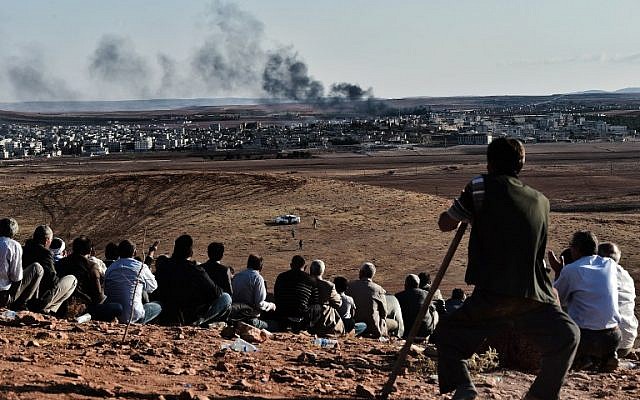 Kurdish people watch smoke billowing from Kobani as they gather upon a hill overlooking the Syrian town of Kobani, also known as Ain al-Arab, in the southeastern village of Mursitpinar, Sanliurfa province, on October 15, 2014.  (photo credit: AFP/ ARIS MESSINIS)