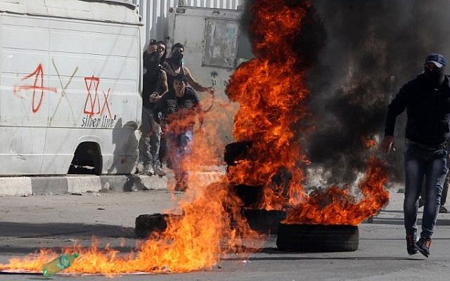 Palestinian protestors stand near burning tires during clashes with Israeli security forces in the West Bank city of Hebron on November 14, 2014 (Photo credit: Hazem Bader/AFP)
