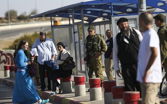 Israelis stand near soldiers on November 11, 2014, at a bus stop at the entrance to the West Bank settlement of Alon Shvut where a Palestinian terrorist killed Dalia Lemkus the day before. (Photo credit: Nati Shohat/Flash90)