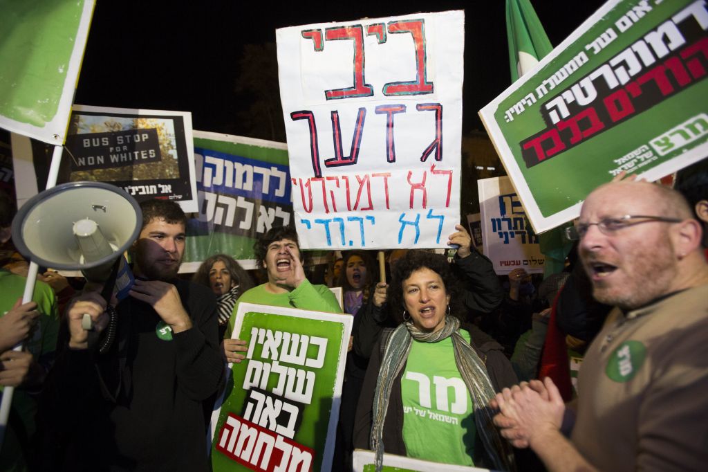 Left-wing activists hold placards and flags as they protest against the 'Jewish state' bill near the Prime Minister residence in Jerusalem on November 29, 2014. Some of the placards call Benjamin Netanyahu a racist, and assert that he seeks democracy for Jews only. (Photo credit: Yonatan Sindel/Flash90)