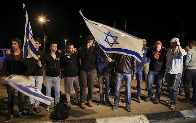 Right-wing Jewish activists wave the Israeli flag as they attend a protest near the site where a young Jewish woman was killed by a Palestinian terrorist, and two people were injured in a stabbing attack at a bus stop at the entrance to the West Bank settlement of Alon Shvut, on November 10, 2014. This is the second terrorist attack of its kind in a day. Earlier today a young Israeli soldier was stabbed by a Palestinian man at a train station in Tel Aviv. (Photo credit: Nati Shohat/Flash90)
