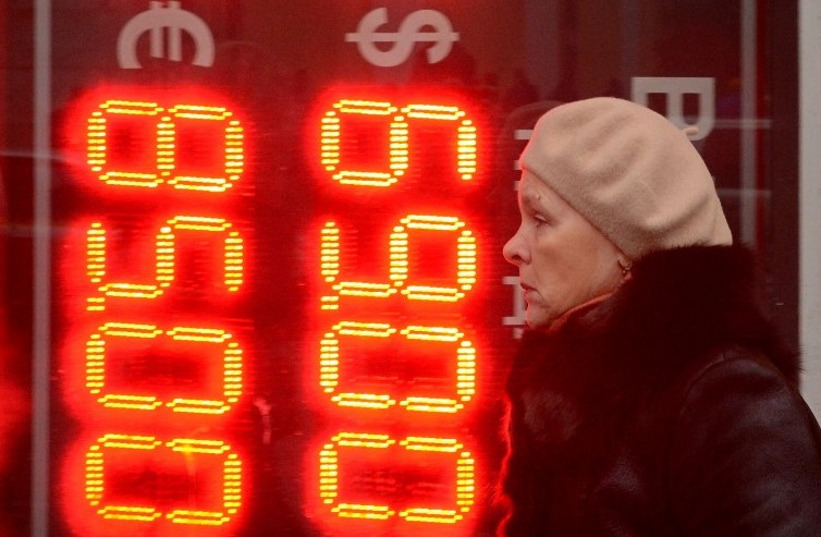 A woman walks past a board listing foreign currency rates against the Russian ruble outside an exchange office in central Moscow on December 16, 2014. (Photo credit: AFP/ Kirill Kudryavtsev)