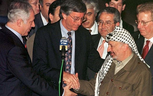Prime Minister Benjamin Netanyahu, US envoy Dennis Ross, and Palestinian Authority president Yasser Arafat clasp hands after initialing an agreement on the partial withdrawal of Israeli troops from the West Bank after a meeting at Gaza's Erez Crossing, Wednesday, Jan 15, 1997. (photo credit: AP Photo/Nati Harnik)