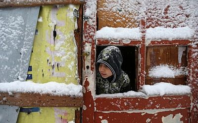 A Syrian boy looks out through his tent door covered in snow at a refugee camp in Deir Zannoun village, in the Bekaa valley, east Lebanon, Wednesday, Jan. 7, 2015. Photo credit: AP/Hussein Malla)