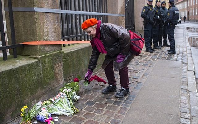 Heavily armed police officers watch a woman laying flowers outside the main synagogue in Copenhagen, Denmark, on February 15, 2015. (photo credit: AFP/Odd Andersen)