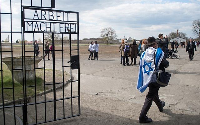 A man with an Israeli flag walks through the gate reading "Arbeit macht frei" (work makes you free) at the entrance to the memorial site of the former Sachsenhausen Nazi concentration camp as he arrives to attend an event to commemorate the 70th anniversary of the camp's liberation, on April 19, 2015 in Oranienburg near Berlin, northeastern Germany. (photo credit: AFP PHOTO / DPA / MAURIZIO GAMBARINI)