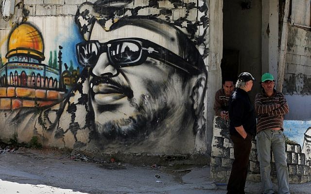 Palestinian refugees stand next to graffiti bearing a portrait of late Palestinian Authority president Yasser Arafat at the Ain Al-Helweh refugee camp, near the southern Lebanese city of Sidon, on March 16, 2015. (AFP/Joseph Eid)