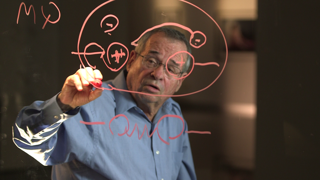 Nobel Laureate Arieh Warshel describing his theory on the see-thru board that Uri Rosenwaks used throughout the five-chapter series (Courtesy Ruth Diskin Films)