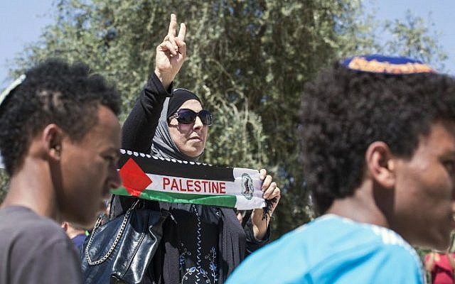 A Palestinian woman holds a scarf bearing the Palestine name as Israeli youth carry their national flag in the "flag march" through Damascus Gate in Jerusalem's Old City during celebrations for Jerusalem Day on May 17, 2015. (AFP Photo/Jack Guez)