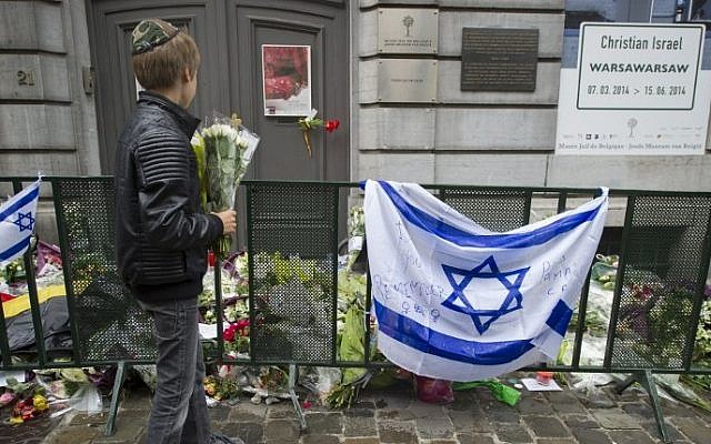 A Jewish boy standing with flowers in front of an Israeli flag and flowers laid outside the Jewish Museum in Brussels, where a deadly shooting took place two days before, May 26, 2014. (AFP/Belga/Anthony Dehez)