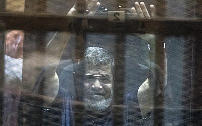Egypt's deposed Islamist president Mohammed Morsi raises his hands from behind the defendant's cage as the judge reads out his verdict sentencing him and more than 100 other defendants to death, at the police academy in Cairo on May 16, 2015. (Khaled Desouki/AFP)