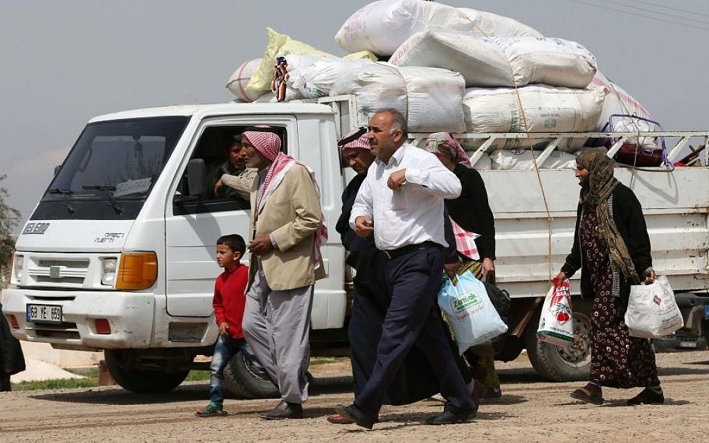 In this picture taken on Monday April 20, 2015, Kurdish refugees who fled from Kobani walk next to a pickup truck full of their belongings on their way to a border gate to return to their town, at the Mursitpinar border crossing in Suruc town, Turkey. (Photo credit: AP/Hussein Malla)