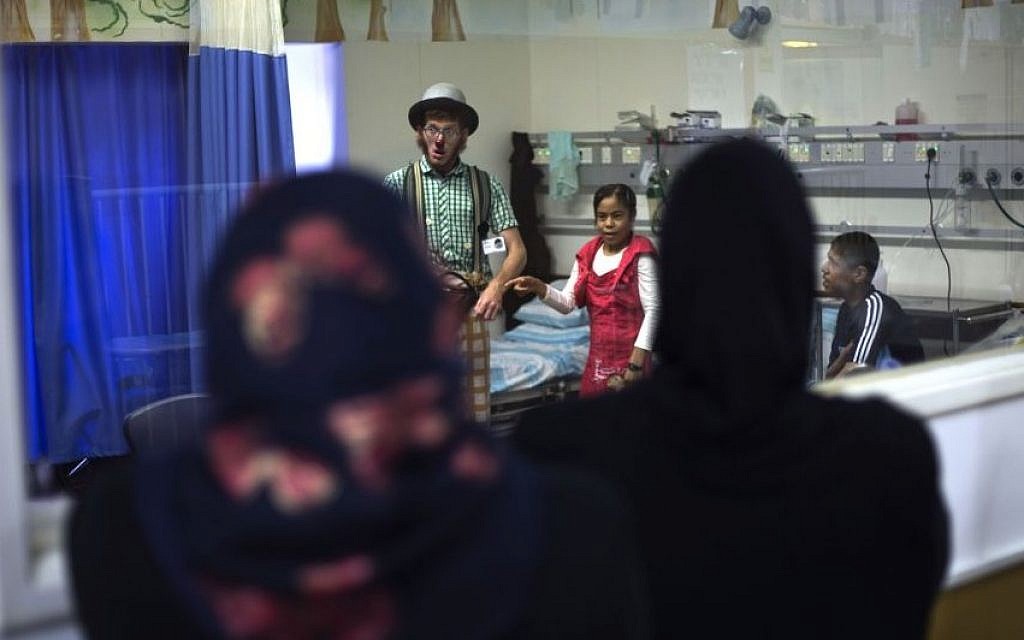 Palestinian siblings Ahmed, right, and Hadeel Hamdan, center, watch ש medical clown who goes by the name 'Juhl' at the Rambam Health Care Campus in Haifa, Israel, May 13, 2015 (AP/Ariel Schalit)