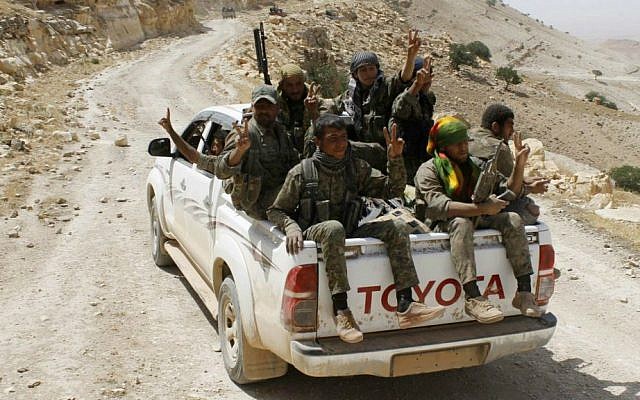 In this photo released on May 20, 2015, provided by the Kurdish fighters of the People's Protection Units (YPG), which has been authenticated based on its contents and other AP reporting, Kurdish fighters of the YPG flash victory signs as they sit on their pickup truck on their way to battle against the Islamic State group, near Kezwan mountain, northeast Syria. (The Kurdish fighters of the People's Protection Units via AP)