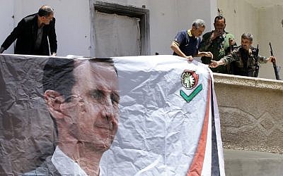 Syrians, including members of the Syrian National Defense Forces (NDF), hang a portrait of President Bashar al-Assad on June 13, 2015 in the ancient Christian town of Maalula, 56 kilometers northeast of the Syrian capital Damascus.  (AFP PHOTO / LOUAI BESHARA)