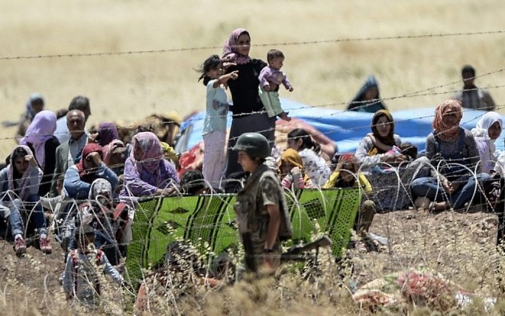 A picture taken from the Turkish side of the border in Suruc, Sanliurfa province, shows Turkish soldiers standing guard (Front) as Syrian Kurds wait behind the barbed wired on the Syrian side after they fled the Syrian town of Kobane, also known as Ain al-Arab, on June 26, 2015, a day after a deadly suicide bombing occurred in the town. At least 120 civilians have been killed by the Islamic State group since it entered the Syrian Kurdish town of Kobane just over 24 hours ago, a monitoring group said. (AFP PHOTO/BULENT KILIC)