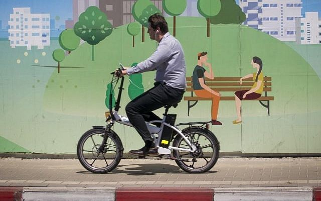 A man rides his electric bike past a mural set up near a construction site in Ramat Gan, near Tel Aviv. April 29, 2015. (Miriam Alster/FLASH90)